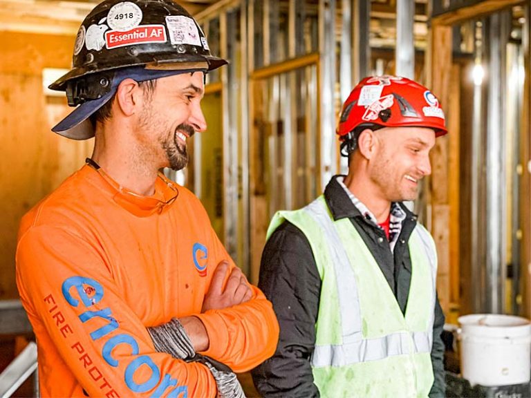 Two Encore technicians in hard hats and safety gear smiling on a construction site